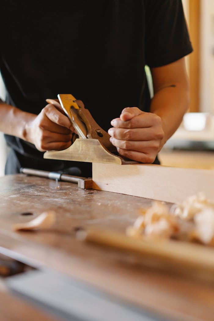 Close-up of a craftsman skillfully planing wood in a workshop. Focus on hand tool and wood shavings.