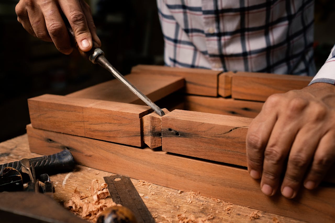 Home Focused view of a person skillfully using a chisel on wooden pieces indoors.